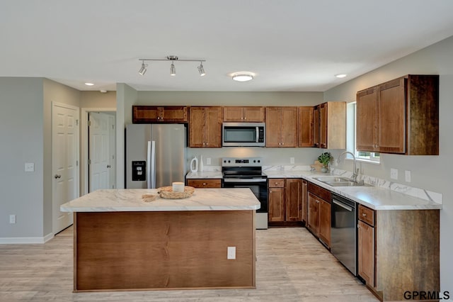 kitchen featuring light wood-type flooring, a center island, appliances with stainless steel finishes, light countertops, and a sink
