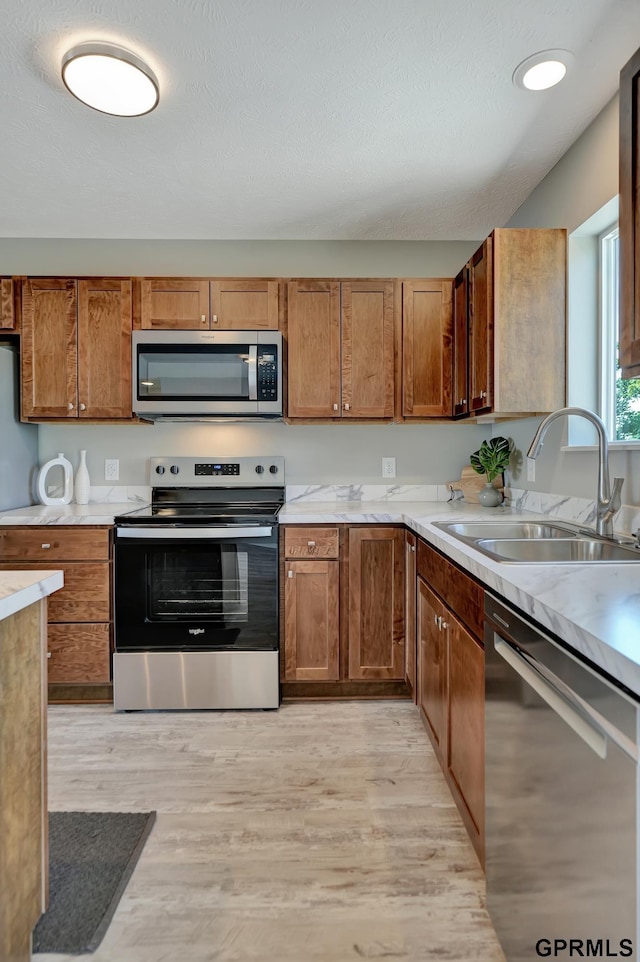 kitchen featuring brown cabinetry, light wood-type flooring, appliances with stainless steel finishes, light countertops, and a sink