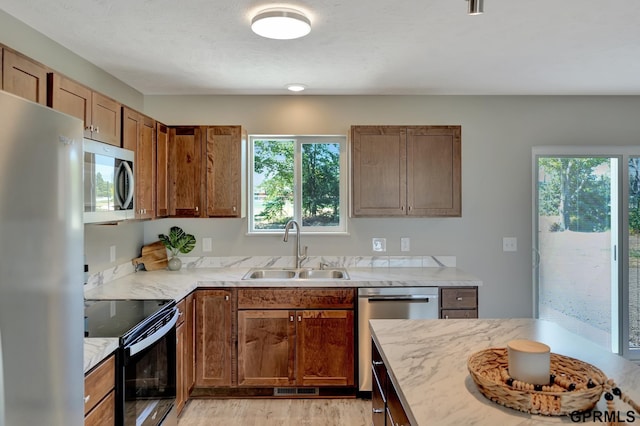 kitchen featuring a sink, brown cabinetry, light wood finished floors, stainless steel appliances, and light stone counters