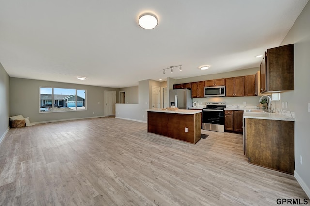 kitchen with a center island, appliances with stainless steel finishes, a sink, light countertops, and baseboards