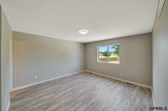 unfurnished room with a textured ceiling, wood finished floors, baseboards, and visible vents