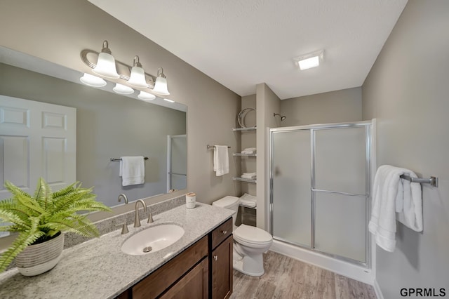 bathroom featuring toilet, vanity, a stall shower, and wood finished floors