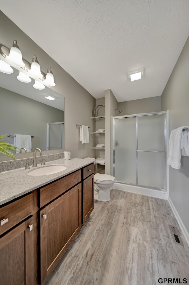 full bathroom with vanity, a stall shower, toilet, visible vents, and wood finished floors