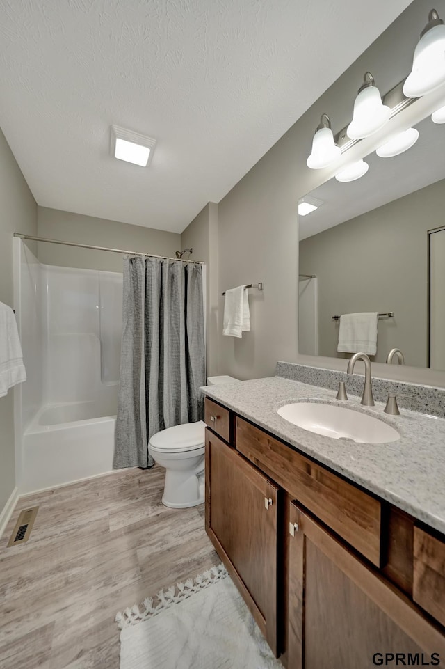 bathroom with visible vents, toilet, shower / bathtub combination with curtain, vanity, and wood finished floors