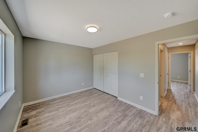 unfurnished bedroom featuring light wood-style flooring, a closet, baseboards, and visible vents