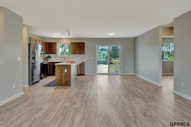 kitchen featuring white microwave, stainless steel fridge with ice dispenser, a center island, light countertops, and range with electric stovetop
