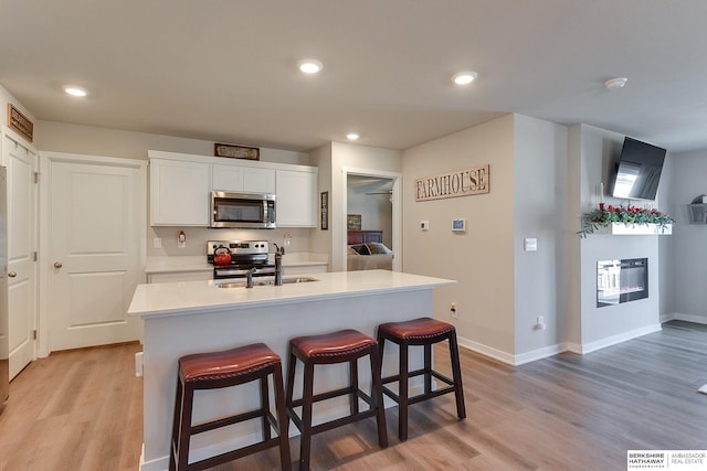 kitchen featuring a glass covered fireplace, light countertops, stainless steel appliances, light wood finished floors, and a sink