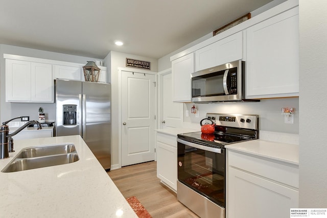 kitchen with light wood-type flooring, white cabinets, appliances with stainless steel finishes, light countertops, and a sink