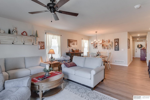 living area featuring visible vents, ceiling fan with notable chandelier, baseboards, and light wood-style flooring