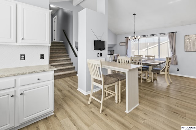 kitchen featuring vaulted ceiling, tasteful backsplash, a chandelier, white cabinets, and baseboards