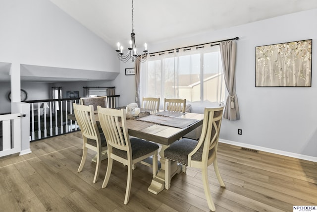 dining area with a chandelier, wood finished floors, baseboards, and high vaulted ceiling