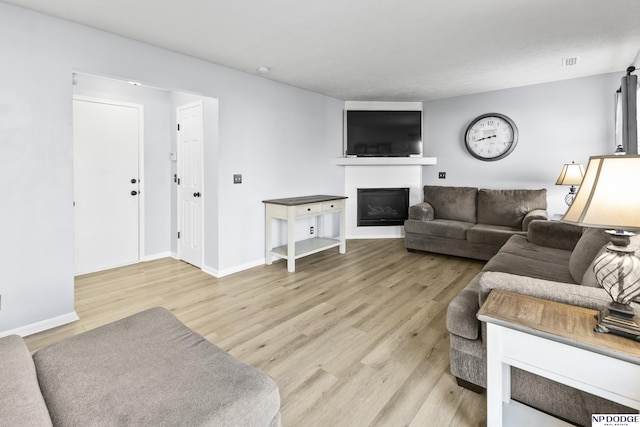 living room with a glass covered fireplace, light wood-style flooring, and baseboards