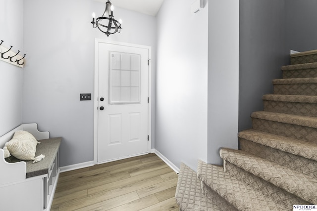foyer featuring stairs, light wood-type flooring, a chandelier, and baseboards