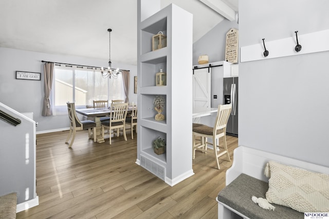 dining area featuring a barn door, light wood-type flooring, a chandelier, and baseboards