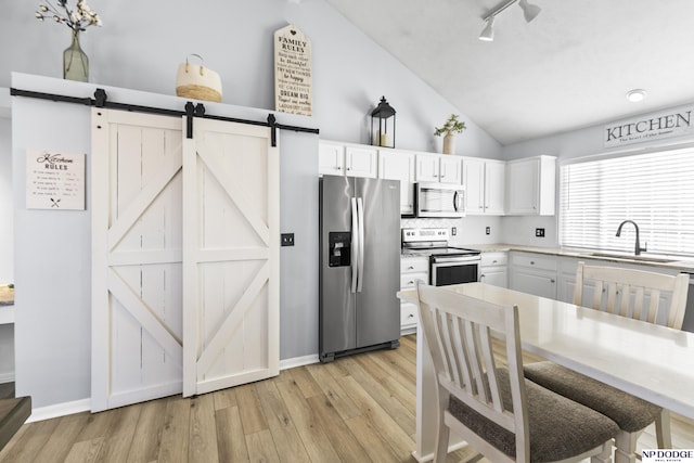 kitchen with appliances with stainless steel finishes, a sink, vaulted ceiling, a barn door, and light wood finished floors