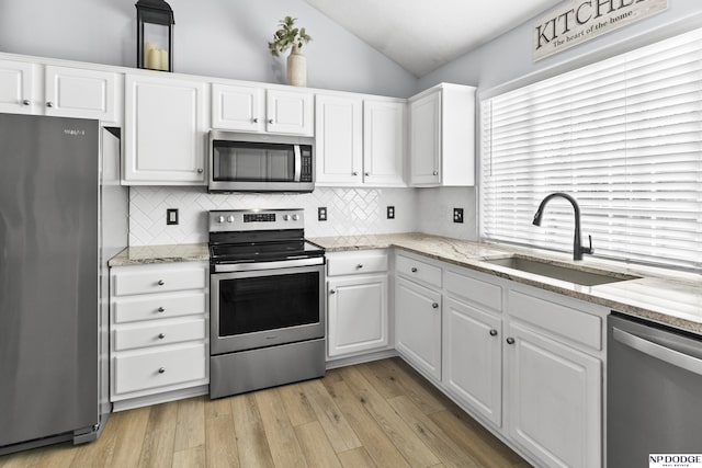 kitchen featuring appliances with stainless steel finishes, a sink, vaulted ceiling, white cabinets, and backsplash