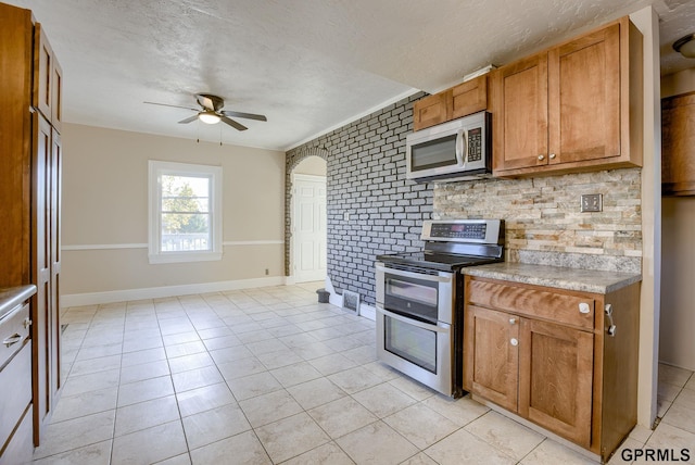 kitchen with light tile patterned floors, a textured ceiling, a ceiling fan, brown cabinets, and stainless steel appliances