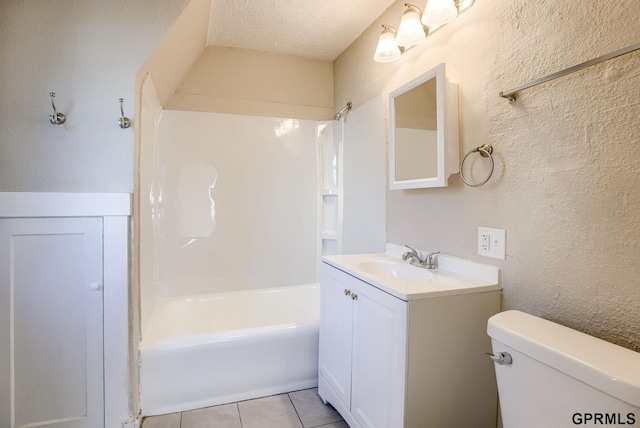 bathroom featuring toilet, a textured wall,  shower combination, vanity, and tile patterned flooring
