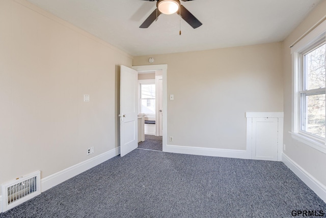 empty room with visible vents, dark carpet, a ceiling fan, and a healthy amount of sunlight