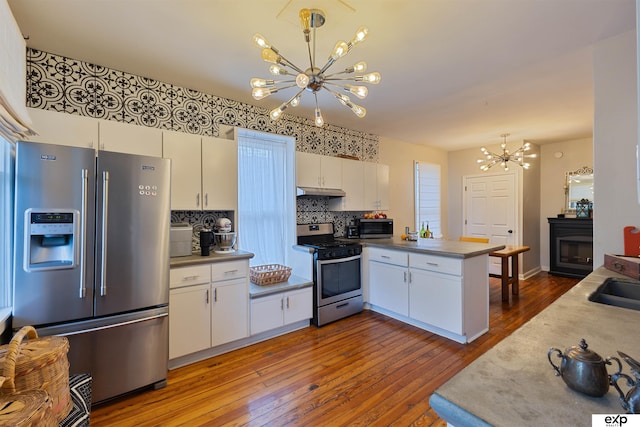 kitchen with white cabinetry, a peninsula, a chandelier, hardwood / wood-style flooring, and appliances with stainless steel finishes