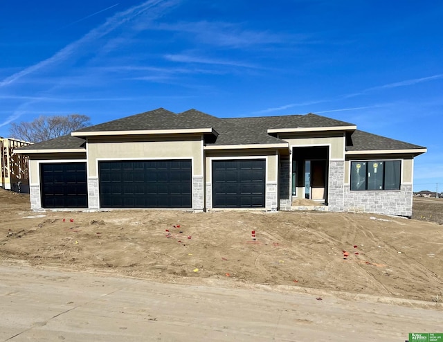 prairie-style home with an attached garage, stone siding, and a shingled roof