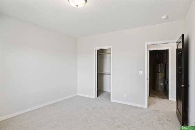 unfurnished bedroom with baseboards, a spacious closet, light colored carpet, and electric water heater
