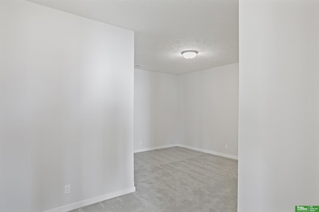 spare room featuring baseboards, a textured ceiling, and light colored carpet