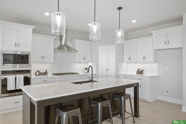 kitchen with stainless steel appliances, a sink, a center island with sink, white cabinetry, and light countertops