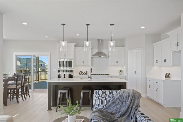 kitchen with wall chimney exhaust hood, a sink, light wood-style floors, stainless steel double oven, and light countertops