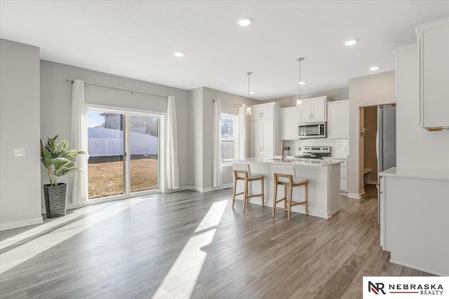 kitchen featuring white cabinets, stainless steel appliances, light wood finished floors, light countertops, and an island with sink