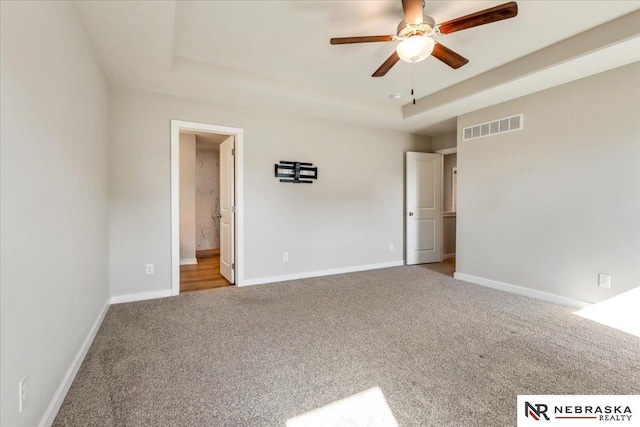 carpeted spare room featuring baseboards, a ceiling fan, a tray ceiling, and visible vents