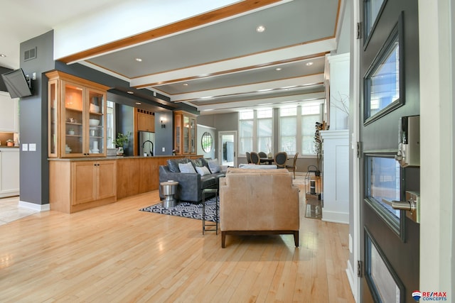living room with beamed ceiling, baseboards, visible vents, and light wood-style floors