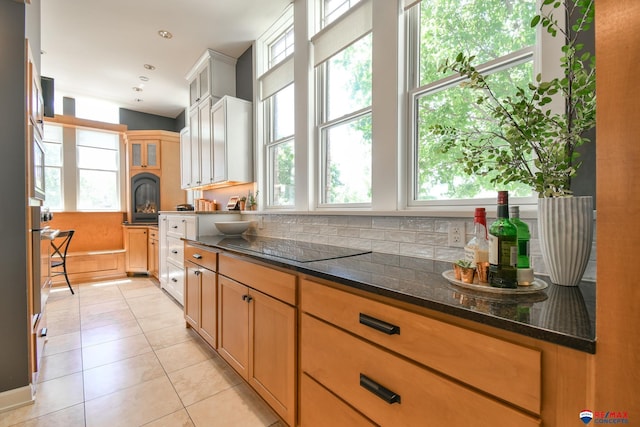 kitchen featuring wall oven, dark stone countertops, glass insert cabinets, black electric stovetop, and light tile patterned floors