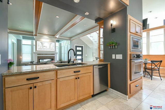kitchen featuring light brown cabinetry, a sink, a high end fireplace, appliances with stainless steel finishes, and light tile patterned floors