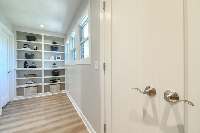 hallway featuring built in shelves, light wood finished floors, and baseboards