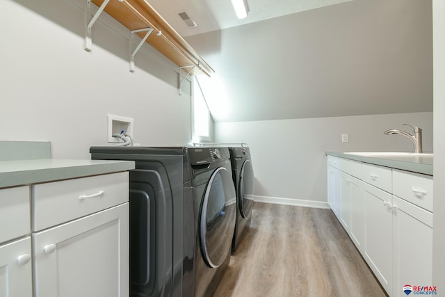 clothes washing area featuring washer and clothes dryer, a sink, light wood-type flooring, cabinet space, and baseboards