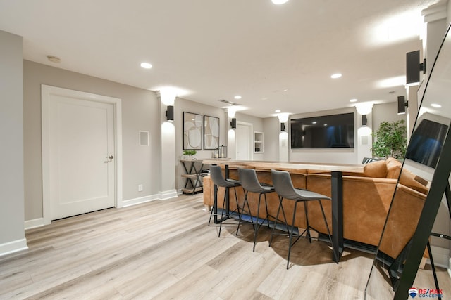 kitchen with recessed lighting, light wood-style floors, baseboards, a peninsula, and a kitchen bar