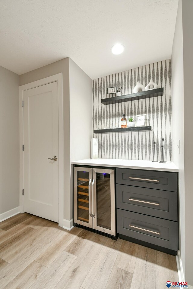 bar featuring baseboards, beverage cooler, light wood-style floors, and a bar
