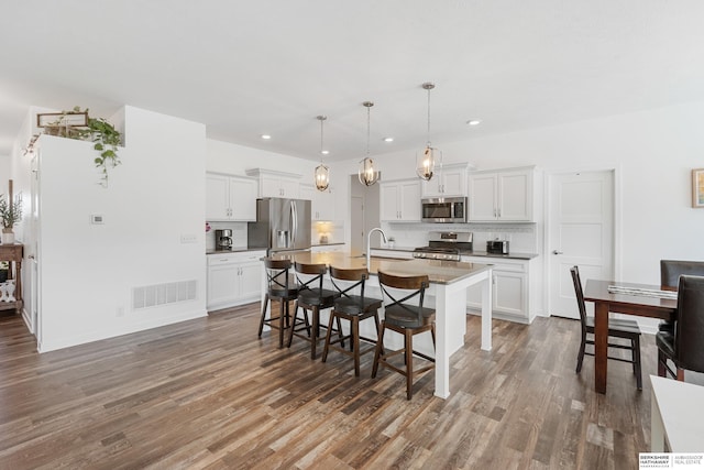 6315 N Hws Cleveland Blvd, Omaha, NE 68116 - kitchen with visible vents, decorative backsplash, wood finished floors, appliances with stainless steel finishes, and a breakfast bar area