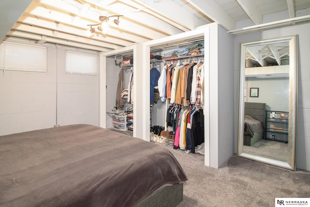 bedroom with concrete block wall, multiple closets, and carpet floors