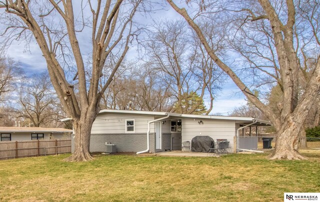 rear view of house with central air condition unit, fence, and a lawn