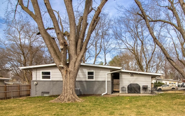 rear view of property featuring brick siding, fence, and a yard