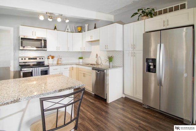 kitchen with appliances with stainless steel finishes, tasteful backsplash, a sink, and dark wood-type flooring