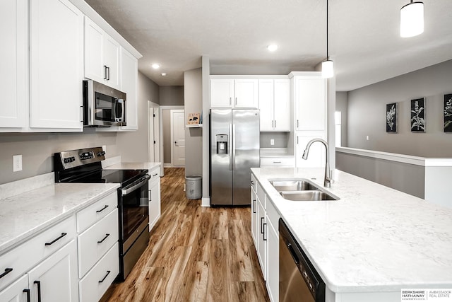 kitchen with white cabinets, a sink, a center island with sink, light wood-style floors, and appliances with stainless steel finishes