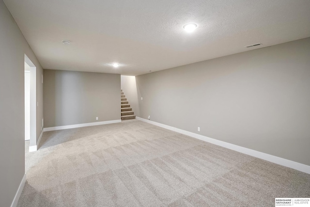 finished basement featuring stairway, baseboards, visible vents, and light colored carpet