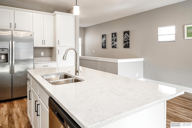 kitchen featuring light wood finished floors, a sink, a kitchen island with sink, appliances with stainless steel finishes, and white cabinetry