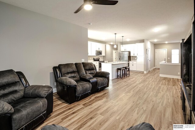 living room with light wood-type flooring, baseboards, and ceiling fan