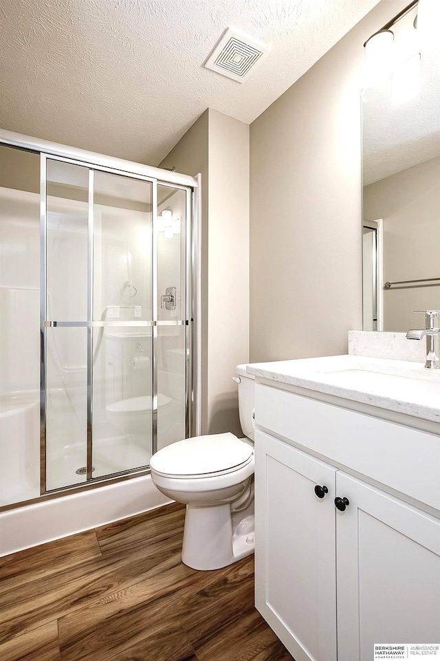 bathroom featuring a shower stall, wood finished floors, vanity, toilet, and visible vents