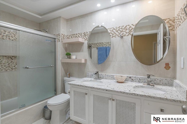 bathroom with double vanity, combined bath / shower with glass door, toilet, and a sink
