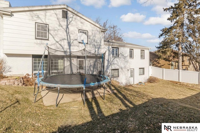 back of property with a trampoline, a lawn, and fence